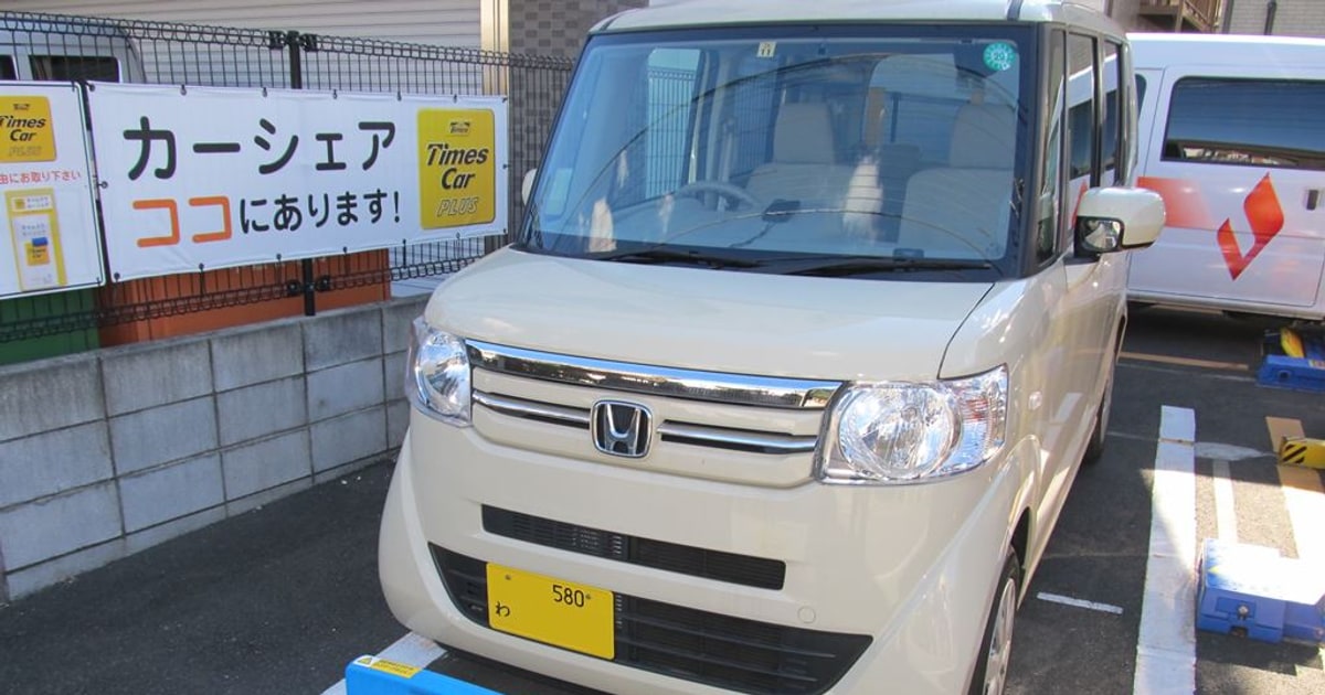Times Car Plus car-sharing vehicle beside a yellow Times sign and a Japanese car-sharing nameboard.